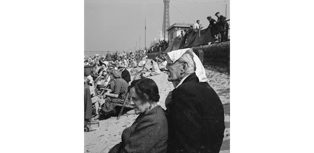 Holiday makers on an crowded beach with an elderly couple in the foreground and Blackpool Tower visible in the distance Date: 1946 - 1955