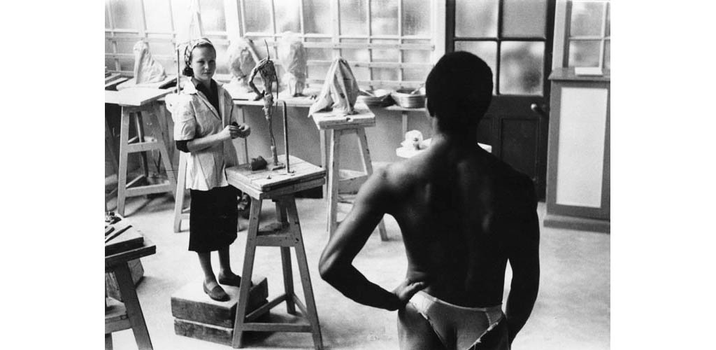 A sculpture student works on a clay model on a tripod, while a nude model poses for her, at the Central School of Art and Design (now Central St Martins College of Art and Design), London. Date: 1957