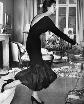 A short sheath dress in black French silk jersey with a deep V back and d飯llet鬠and a swirling hem of black taffeta, designed by Neil (Bunny) Roger, in whose house the photograph was taken, at Fortnum and Mason. Date: 1956