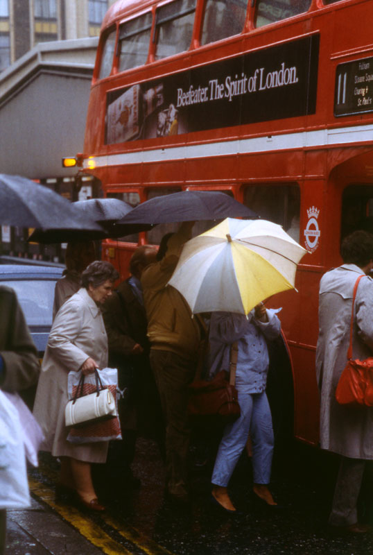 London Street Scene -- people with umbrellas crowding to get onto a number 11 bus on a rainy day.
1960s