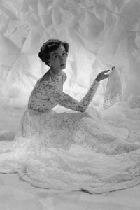 A frothy confection of lace designed by Victor Stiebel (1907-1976). Dress has the typical fitted bodice of the fifties and billowing skirt. Model holds lace handkerchief. Date: 1950s