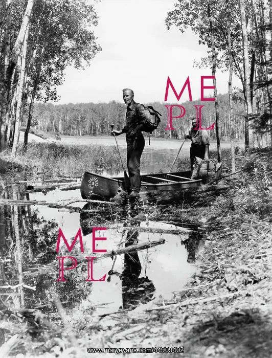 : 1930s 1940s two men standing in canoe in shallow : 1930s 1940s two men standing in canoe in shallow