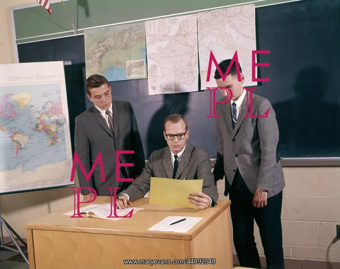 : 1960s TEACHER SITTING AT DESK WITH BOY STUDENTS : 1960s TEACHER SITTING AT DESK WITH BOY STUDENTS