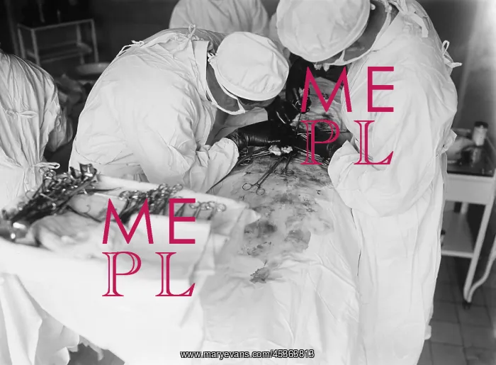 : Attending surgeon leans over to work closely over : Attending surgeon leans over to work closely over