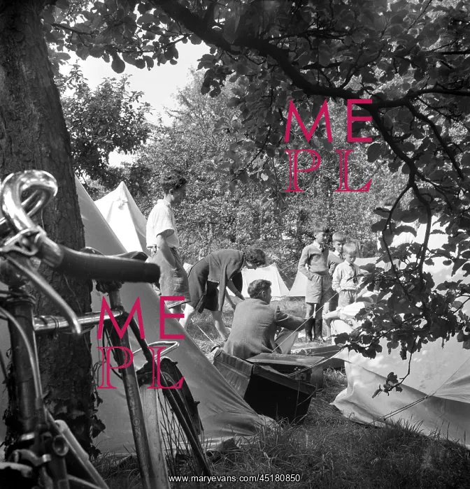: Camping. Looking past a bicycle propped against a tree, towards a group of people camping : Camping. Looking past a bicycle propped against a tree, towards a group of people camping