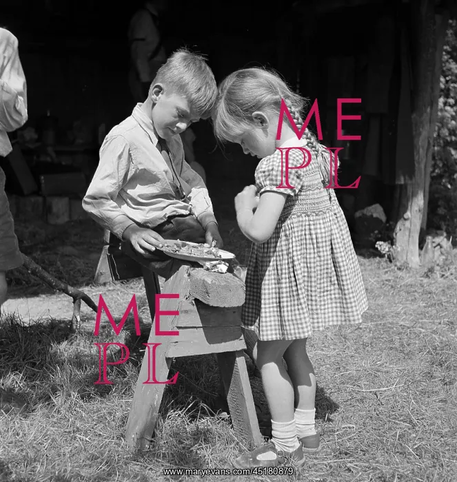 : Children. A young girl standing next to a boy sitting on a sawhorse with a plate of food : Children. A young girl standing next to a boy sitting on a sawhorse with a plate of food