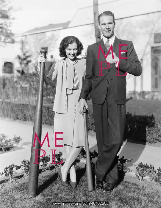 : Couple standing together with one oversized baseball bat : Couple standing together with one oversized baseball bat