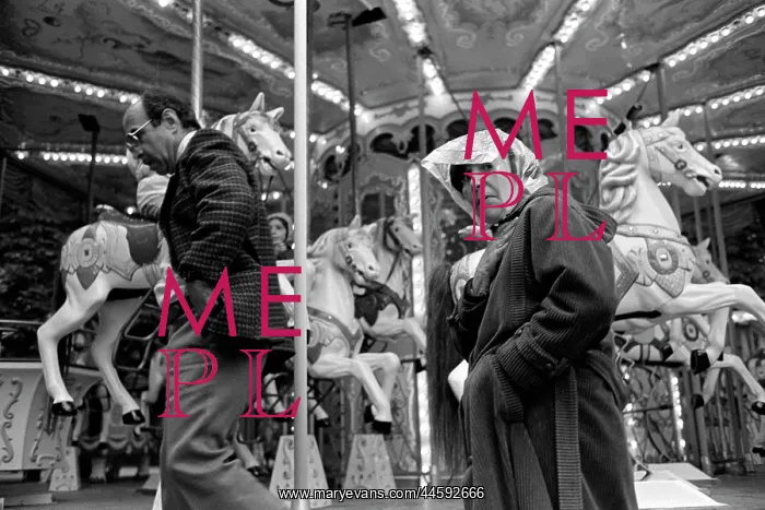 : A couple walk past a fairground carousel : A couple walk past a fairground carousel