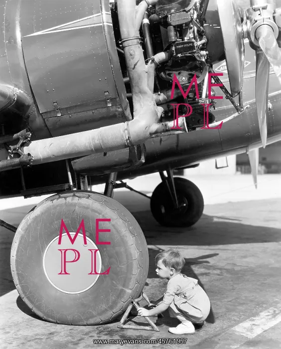  : Little boy crouching by the wheel of a plane