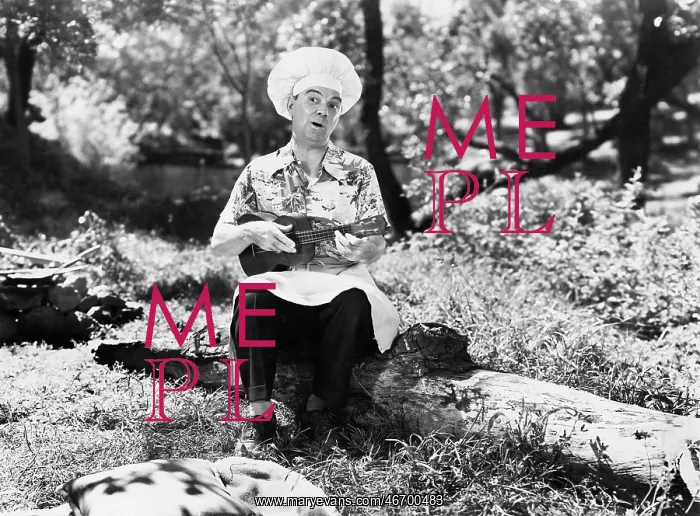 : Man in a chefs hat sitting outside and playing the ukulele : Man in a chefs hat sitting outside and playing the ukulele