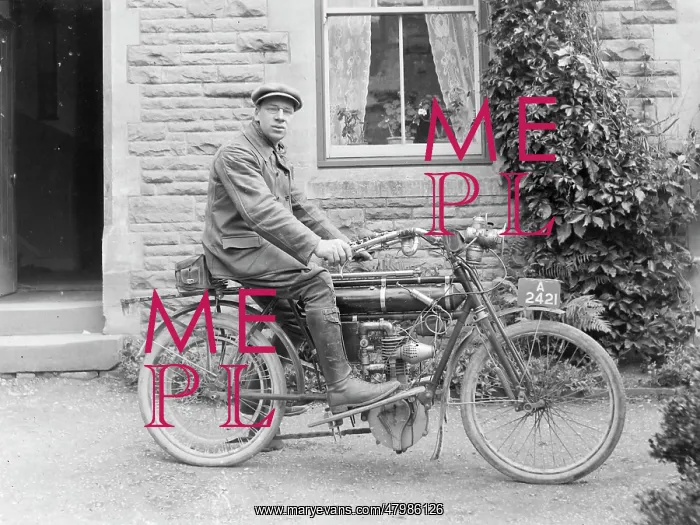 : Man on an early motorcycle in front of a house : Man on an early motorcycle in front of a house