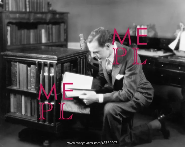 : Man kneeling in his home library browsing a book : Man kneeling in his home library browsing a book