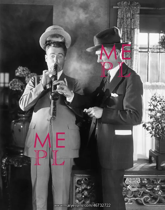: Man lighting a long pipe while his hat is lifting : Man lighting a long pipe while his hat is lifting