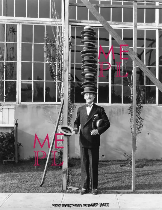 : Man standing with stack of hats on head : Man standing with stack of hats on head