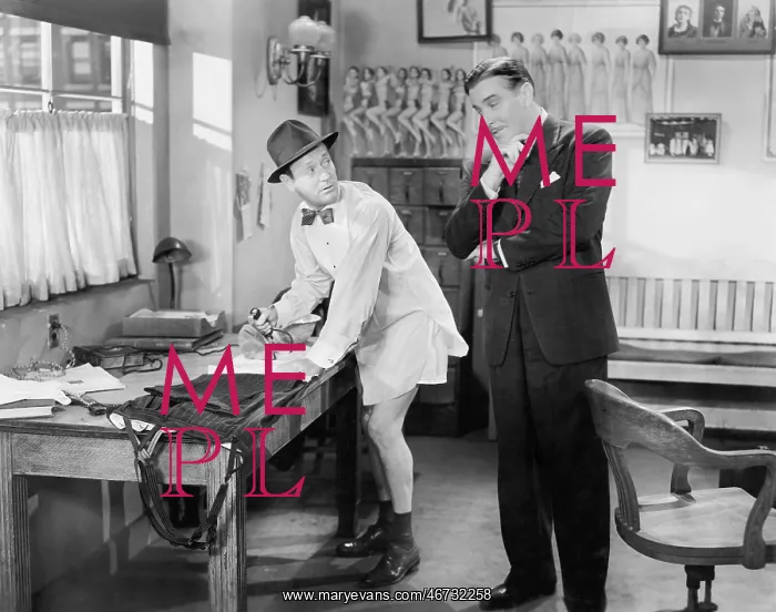 : Two men standing in an office, one ironing his pants : Two men standing in an office, one ironing his pants