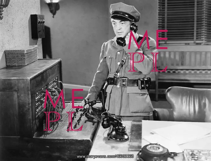 : Officer talking on a telephone next to a switchboard : Officer talking on a telephone next to a switchboard