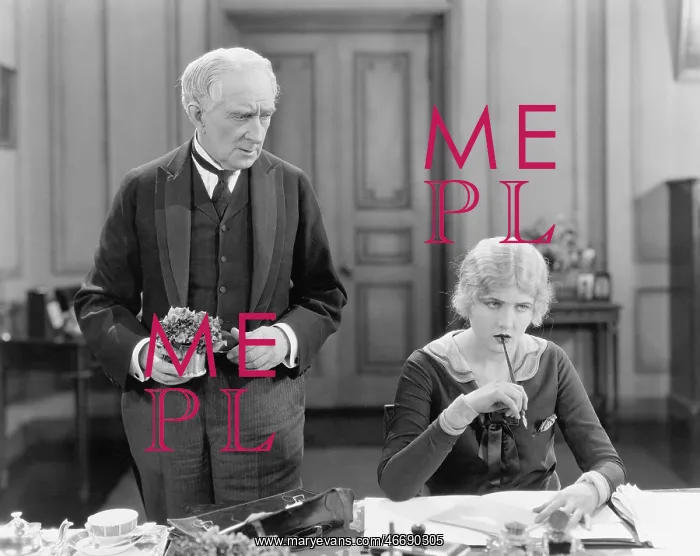 : Older man standing next to a woman at her desk : Older man standing next to a woman at her desk