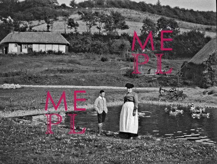 : Woman and boy standing by a duckpond : Woman and boy standing by a duckpond