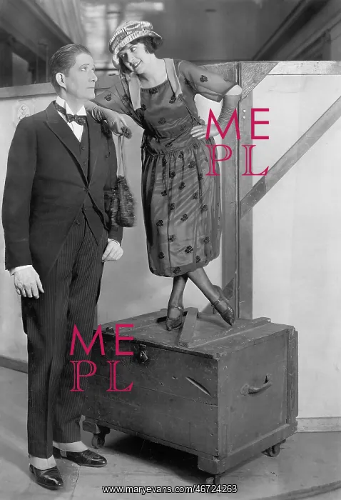 : Woman standing on a trunk next to a very tall man : Woman standing on a trunk next to a very tall man