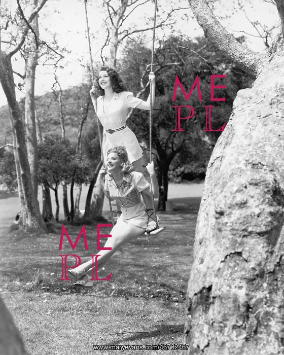 : Two women sitting and standing on a swing : Two women sitting and standing on a swing