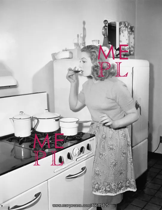 : Young woman in an apron in her kitchen tasting her : Young woman in an apron in her kitchen tasting her
