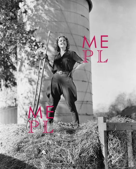 : Young woman standing on a haystack and holding a pitchfork : Young woman standing on a haystack and holding a pitchfork
