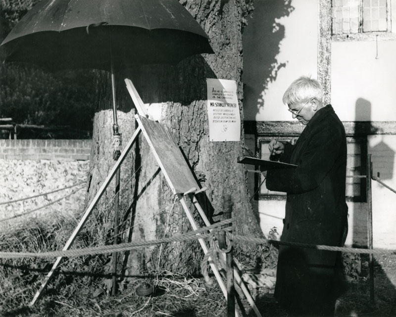STANLEY SPENCER (1891-1959), English artist, photographed in profile whilst at work on his painting of Cookham Churchyard, Berkshire, England. Date: 1958