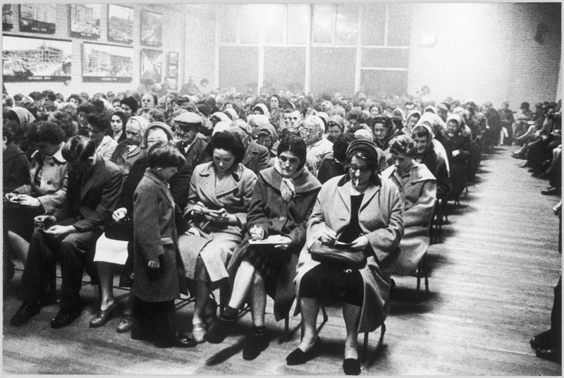 A small boy on the front row is intrigued by women with "eyes down" for bingo on the front row at the Old People's Club on the Park Hill Estate, Sheffield, Yorkshire, England. Date: 1961