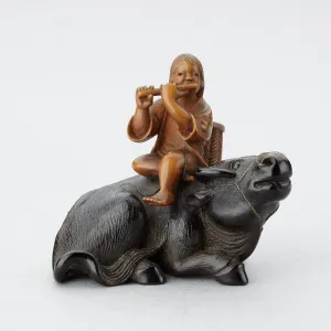 Netsuke of a oshikyo sitting on an ox playing the flute Netsuke of a oshikyo sitting on an ox playing the flute