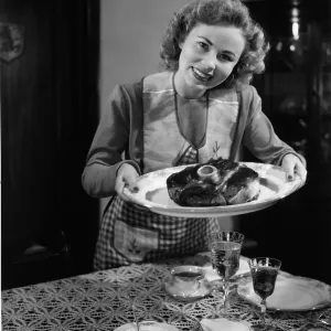 Woman in apron serving up a plate of cooked ham Woman in apron serving up a plate of cooked ham