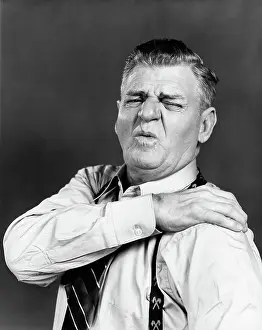 Grimacing: 1940s ELDERLY MAN GRIMACING AND HOLDING SHOULDER