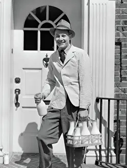 Milkmen: 1940s MILKMAN SMILING AT CAMERA ON DOORSTEP DELIVERING
