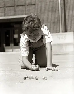 Knuckle: 1950s SMILING BOY READY TO SHOOT KNEELING ON