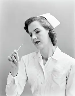 Providers: 1950s woman nurse checking temperature on thermometer?