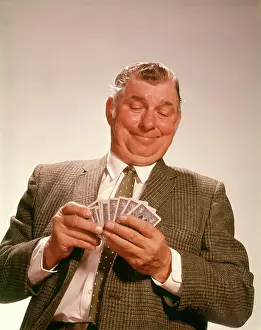 Dealt: 1960s SMILING SATISFIED MAN LOOKING AT HAND OF