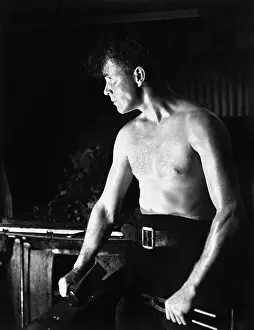 Upward: Bare chested man sitting and holding tools in his hands