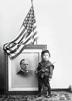 1890 1899: Boy in sailor uniform standing by a portrait