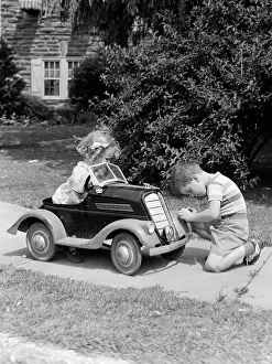 Well Kept: Boy on sidewalk fixing headlight of toy car driven