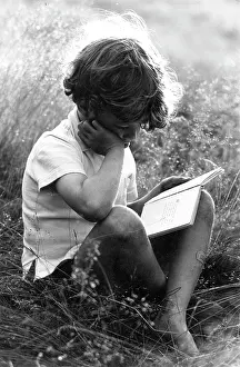 Summers: Boy sitting in sunlit long grass reading