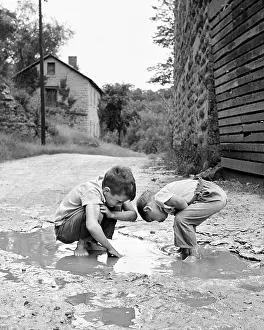 Two Boys Bending Looking at Playing in Mud Puddle