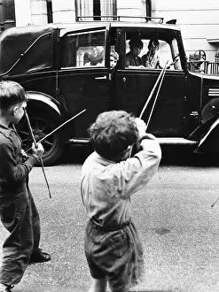 Londonroger: Boys playing bows and arrows with a car