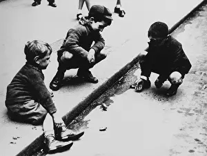 Marbles: Three boys playing marbles in the gutter