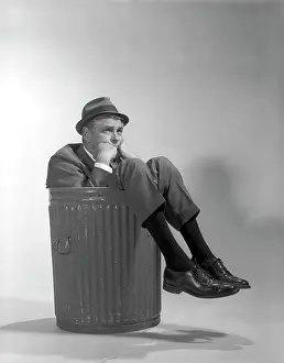 Businesspeople: Businessman in suit and hat sitting in trashcan