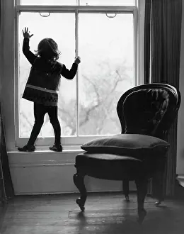 Child silhouetted standing at a large sash window