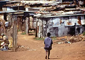 Shacks: A child walks along a dirt road towards corrugated