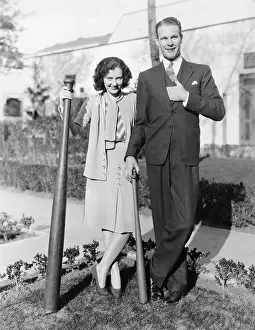 Oversize: Couple standing together with one oversized baseball bat