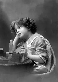 Contemplating: A curly-haired boy playing with wooden building bricks