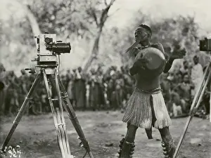 Rattles: Dancer with leg rattles and hand drum in front of
