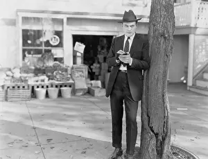 Fedora: Detective leaning against tree taking notes
