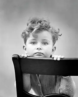 Unfamiliar: Diffident Curly Hair Boy Resting Chin on back of Chair